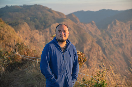 Asian fat man with beautiful sunrise of khao San nok wua mountain kanchanaburi.Khao San Nok Wua is the highest mountain in Khao Laem National Park. It is 1767 meters above sea level.の写真素材