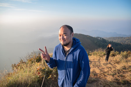 Asian fat man with beautiful sunrise of khao San nok wua mountain kanchanaburi.Khao San Nok Wua is the highest mountain in Khao Laem National Park. It is 1767 meters above sea level.の写真素材