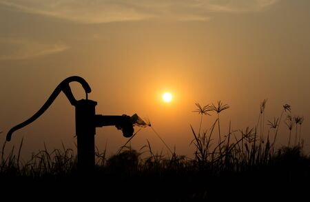 The silhouette water pump on the grass and rice field with the sun on the evening , with copy spaceの写真素材