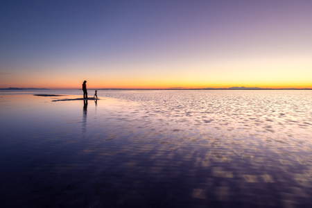Photographer standing in the shallow water at dawn, Bonneville Salt Flats near Great Salt Lake, Utahの写真素材