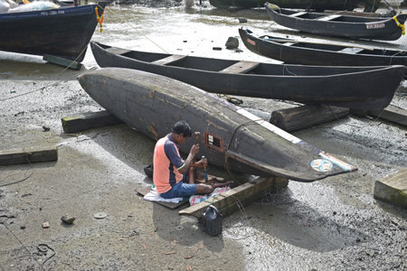Unidentified fisherman is repairing his boat on the beach.の写真素材