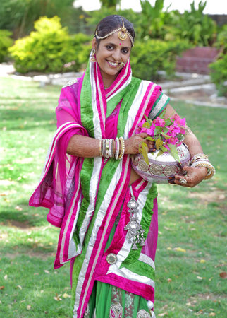 Beawar, Rajasthan, India, April 9, 2016: Portrait of a smiling rajasthani young woman in traditional attire with silver pot poses for a picture on Gangaur festival in Beawar. Photo: Sumit Saraswat