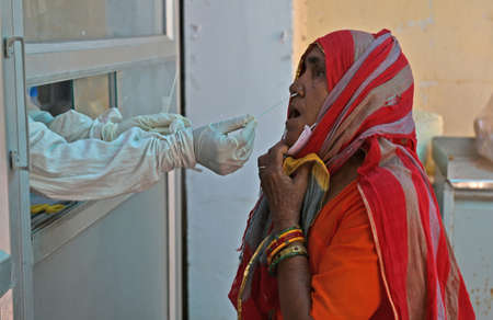 Beawar, Rajasthan, India, May 10, 2021: A health worker collects swab sample from a village woman at a COVID-19 testing lab during second wave of coronavirus epidemic, in Beawar. Photo: Sumit Saraswatのeditorial素材