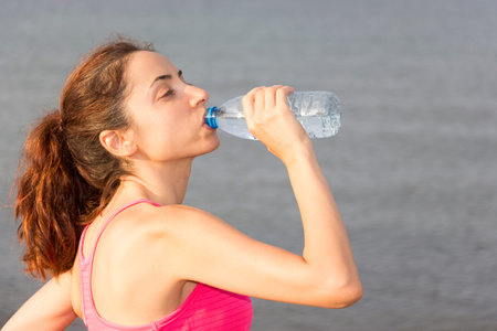 Woman is drinking water outdoors.