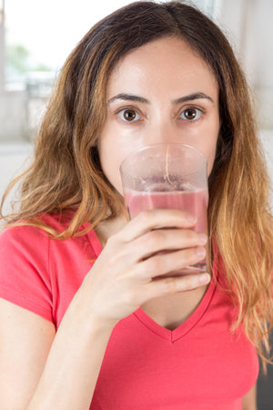 Caucasian woman drinking a glass of berry smoothie.