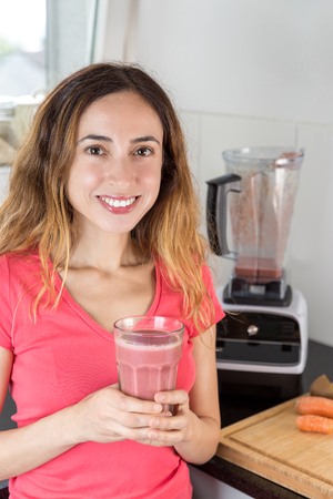 Happy healthy woman with a glass of smoothie in her hands in the kitchenの写真素材