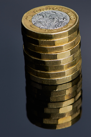 A column of used British one pound sterling coins with reflection below in black glassの写真素材