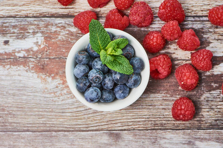 top view on blueberries in a white bowl with some peppermint in the middle of a wooden background,...