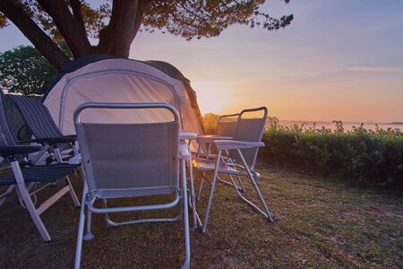 camping table with chairs and a tent standing on a campsite in front of a sunrise in Franceの写真素材