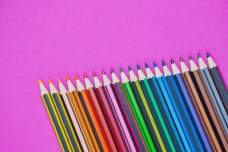 row of different colored pencils on a pink background with copy spaceの写真素材
