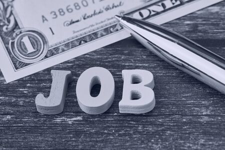 black and white photo of the English word - job - laid with wooden letters beside a ballpoint pen and part of a one dollar billの写真素材