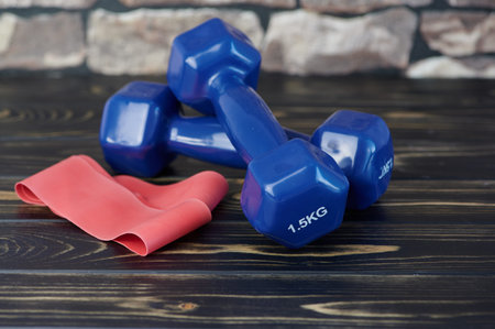 red elastic exercise band beside blue dumbbells on wooden surface