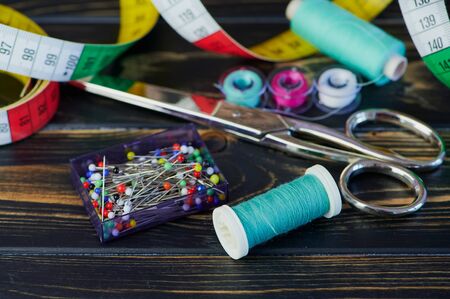 macro color photo of different sewing tools like scissors and sewing thread on wooden tableの写真素材