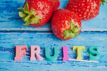 the word: fruits laid with colored wooden letters beside fresh strawberries on blue backgroundの写真素材