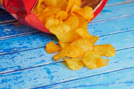 potato chips lying in front of a chips bag against blue backgroundの写真素材