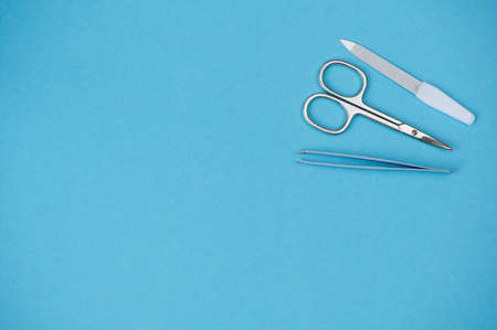 Nail scissors, tweezers and nail file are on the right side on blue background, copy space for any textの写真素材