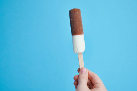 vanilla ice cream with chocolate on a stick held by a childs hand, with copy space