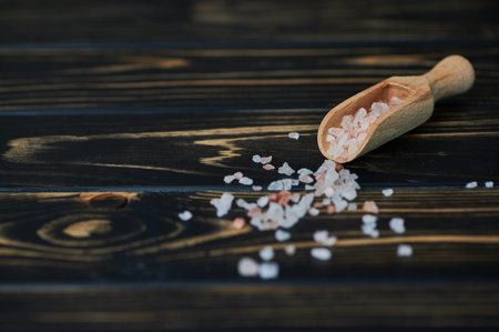Himalayan salt in a small wooden scoop on dark background with copy spaceの写真素材