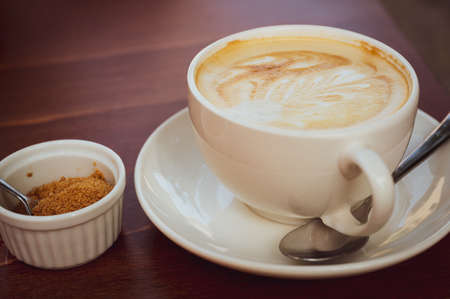 coffee with frothed milk with great leaf pattern, next to it is raw cane sugar, selective focus on the middle of the cupの写真素材