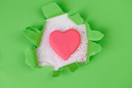 green torn paper, in the middle is lying a pink heart made from plasticine as symbol for health careの写真素材