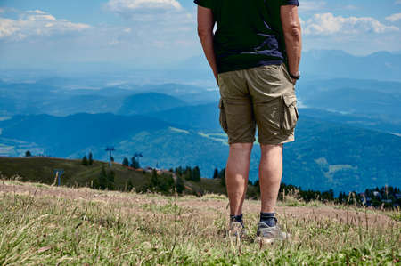 Adult man in shorts stands on top of Gerlitzer Alpe and looks at mountain landscape in Austriaの写真素材