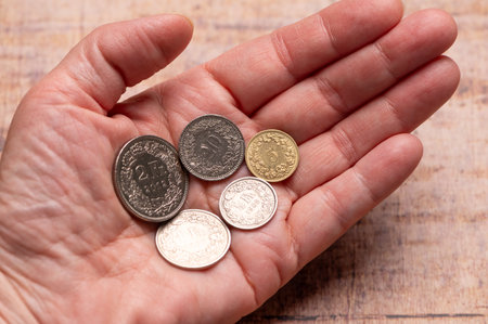Different Swiss Franc coins balanced in an open palm on a smooth wood.の写真素材