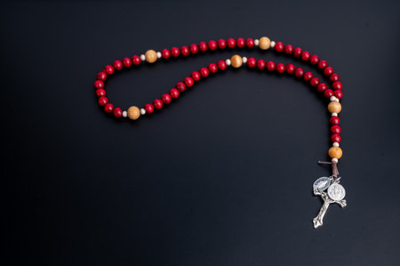 Red wooden rosary with silver cross on black surface.の写真素材