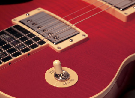 The detail of a red electric guitar showing strings, pickup and rhythm/treble switch