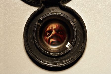 Looking through the peephole of an apartment door at an angry fellow on the other side.の写真素材
