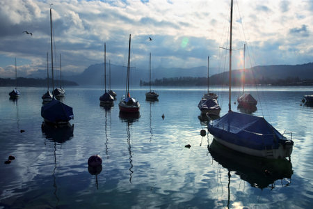 Group of sailboats anchored near the dock just as the sun starts to set.  Lens flare visible.  Taken...