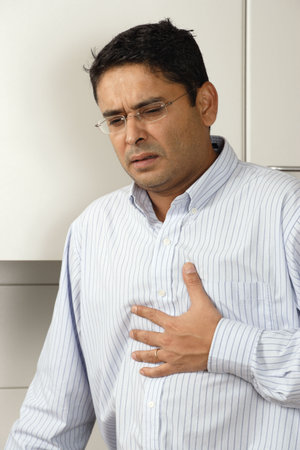 Man in his late thirties standing in his kitchen having a dose of heartburn after a meal.