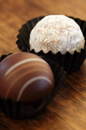 Photo of two chocolate truffles in paper wrappers.  Very Shallow depth of field, focusing on white...