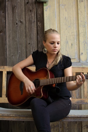 Photo of a beautiful blond female playing her acoustic guitar on an old wooden bench.  の写真素材