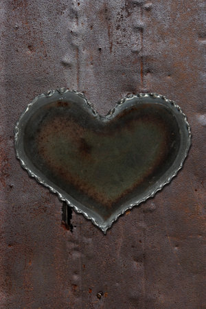 Photo of a metal heart attached to a sheet of rusty sheet metal.の写真素材