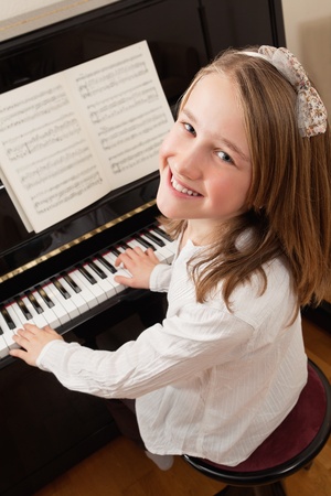 Photo of a young girl playing the piano at home. Sheet music has been altered to be unrecognizable.の写真素材