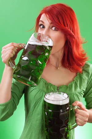 Photo of a beautiful redhead holding two huge mugs of green beer and drinking from one, on St. Patricks Day.の写真素材