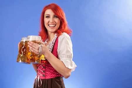 Photo of a beautiful female waitress wearing traditional dirndl and holding two mass beer steins.の写真素材
