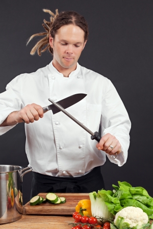 Photo of a chef with dreadlocks sharpening his chopping knife.の写真素材