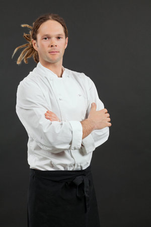 a male chef with dreadlocks, standing with his arms crossed over dark background 