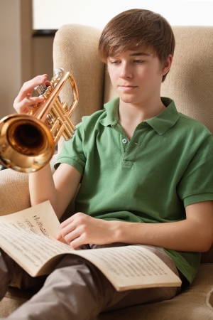 Photo of a teenage male reading sheet music and practicing his trumpet at home.の写真素材