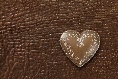 Photo of a metal heart on a dark brown leather background.の写真素材