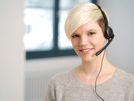 Photo of a cute young call center female with short blond hair and big smile wearing a headset.の写真素材