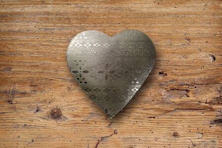 Photo of an ornate metal heart on top of an old plank of wood の写真素材