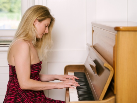 Photo of a happy blond female in her early thirties playing the piano at home.の写真素材
