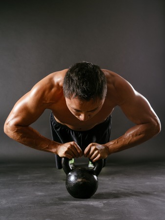 Photo of a muscular Asian man doing pushups with a kettlebell の写真素材