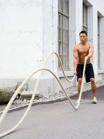 Photo of a muscular Asian man working out with training ropes の写真素材
