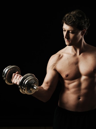 a man in his early thirties doing bicep curls with a dumbbell over a black.の写真素材