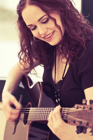 Photo of a woman playing an acoustic guitar by a window. Heavily filtered.の写真素材