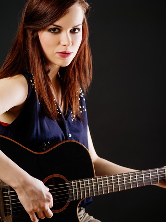 Photo of a beautiful brunette female playing an acoustic guitar over black background.の写真素材