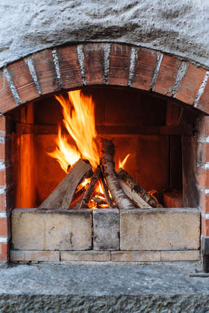 Photo of an outdoor brick fireplace with a fire blazing inside.の写真素材